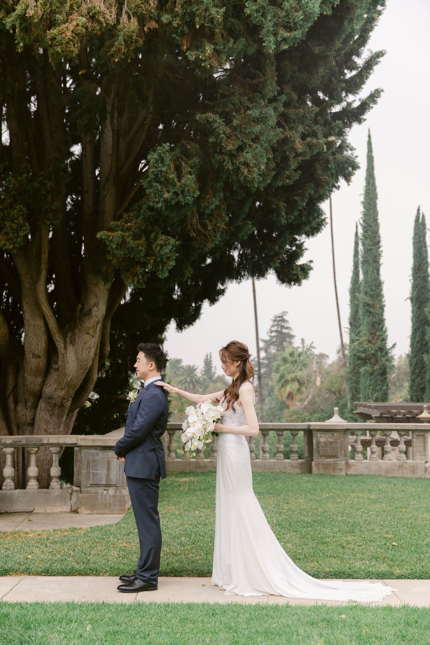 A romantic first look moment captured in a garden with tall cypress trees.