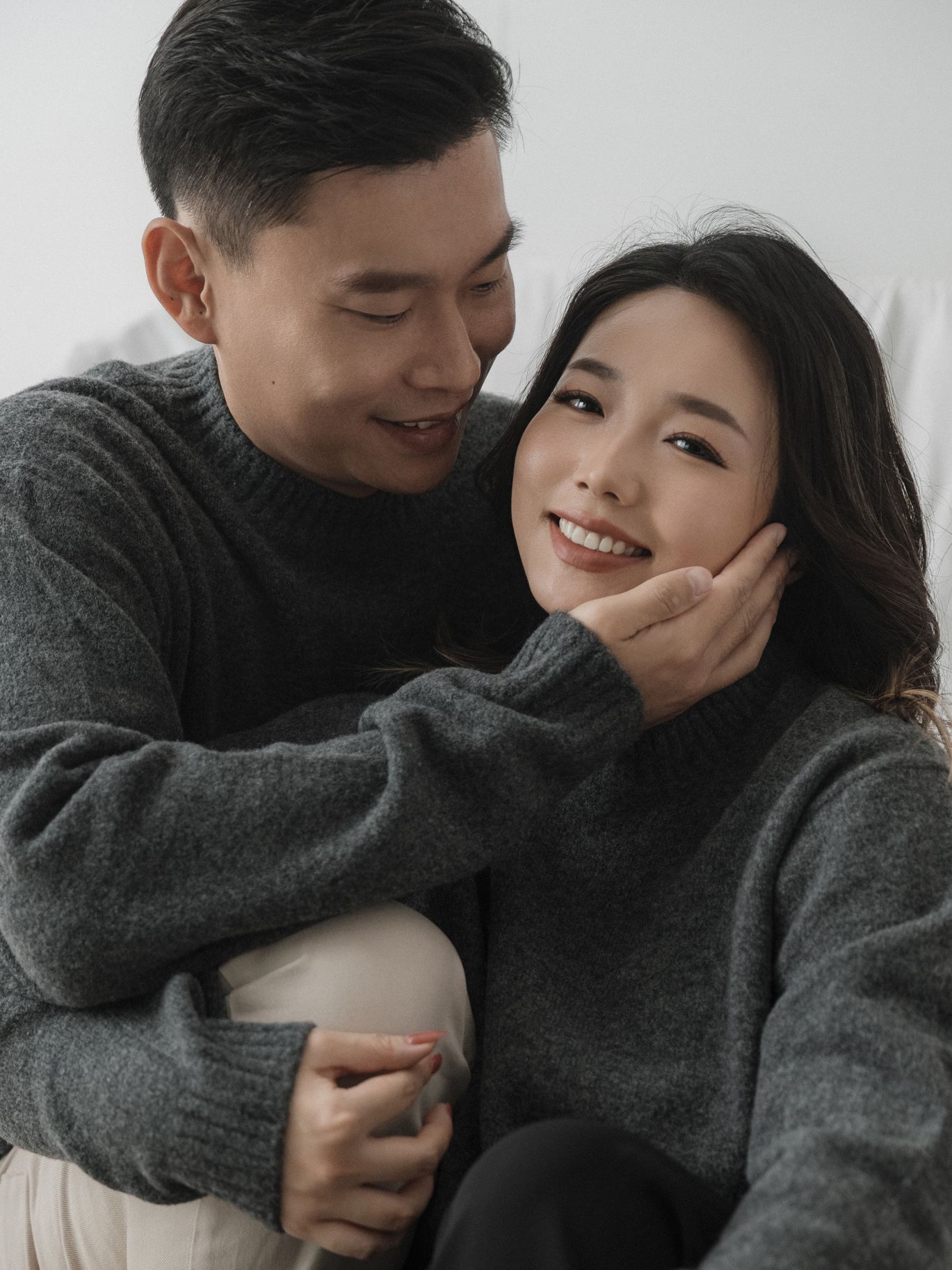 Playful couple embracing and laughing in matching gray sweaters.
