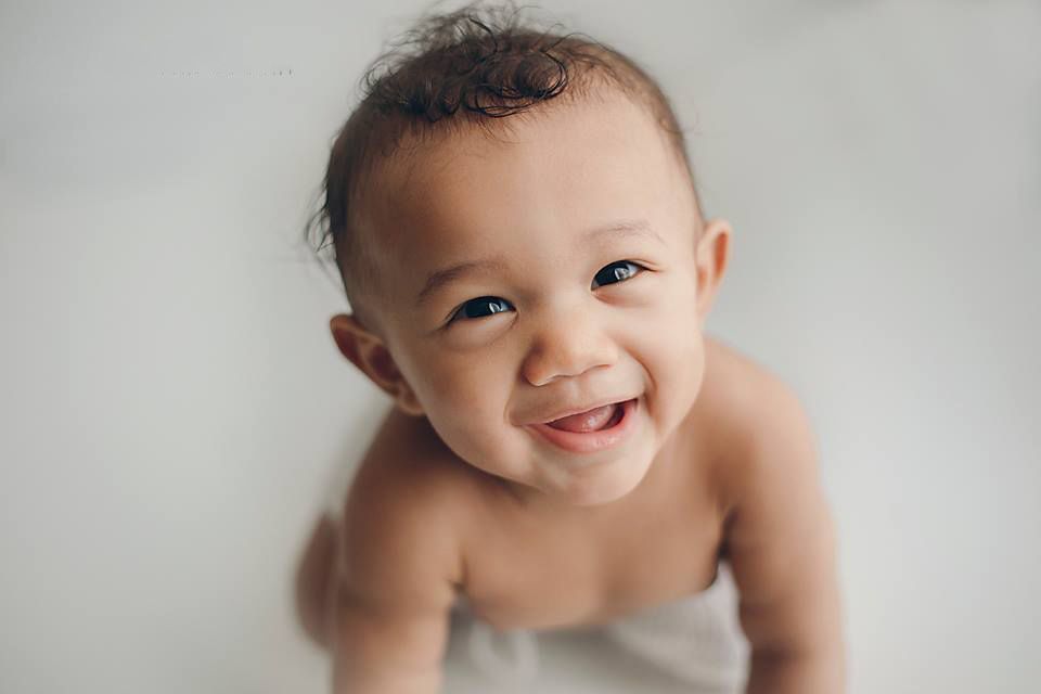 Smiling baby boy with dark hair looking up at camera against soft white background Richmond family photographer, midlothian, glen Allen,