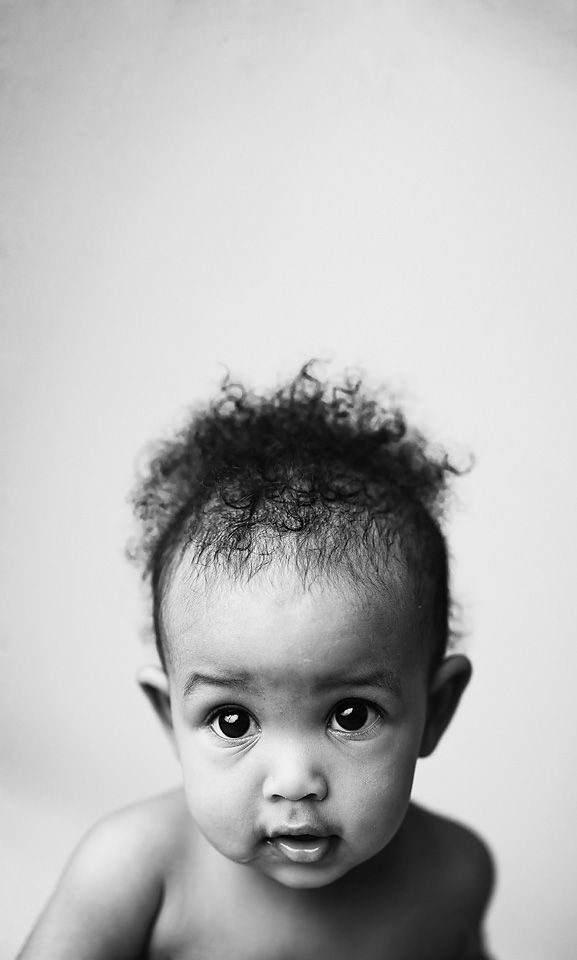 Close-up black and white portrait of a curly-haired baby with expressive eyes on white background.