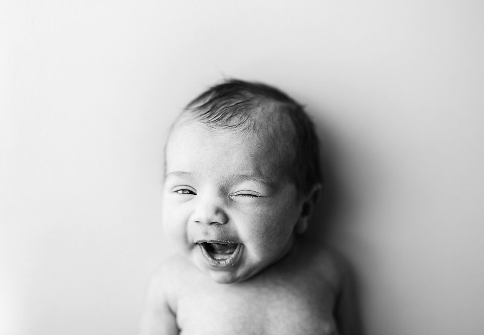 Black and white photo of a laughing newborn baby with eyes closed, showing pure joy and happiness.