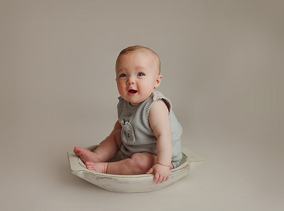 Adorable baby boy in sage green romper sitting in bowl prop during milestone photo session.