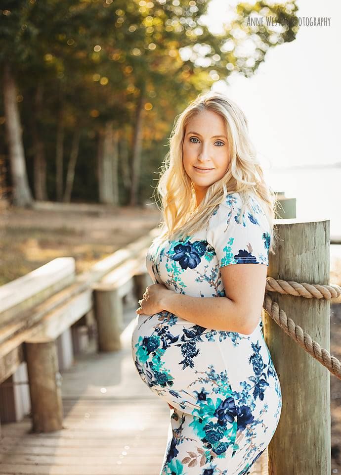 Pregnant woman in floral dress poses on wooden dock by water during golden hour maternity photoshoot. Richmond, Petersburg, Midlothian
