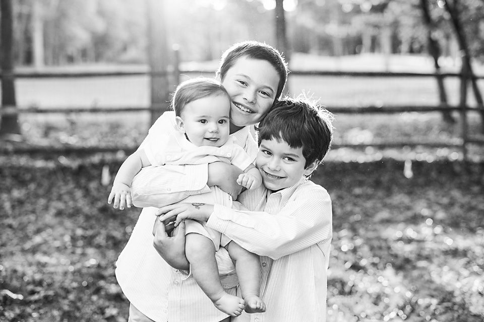 Black and white portrait of three siblings, older girl holding a baby with a boy nearby.