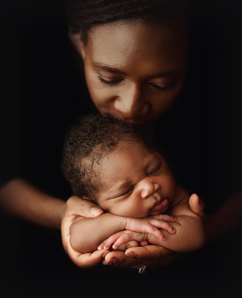 Tender portrait of a mother lovingly kissing her sleeping newborn baby held in her hands.