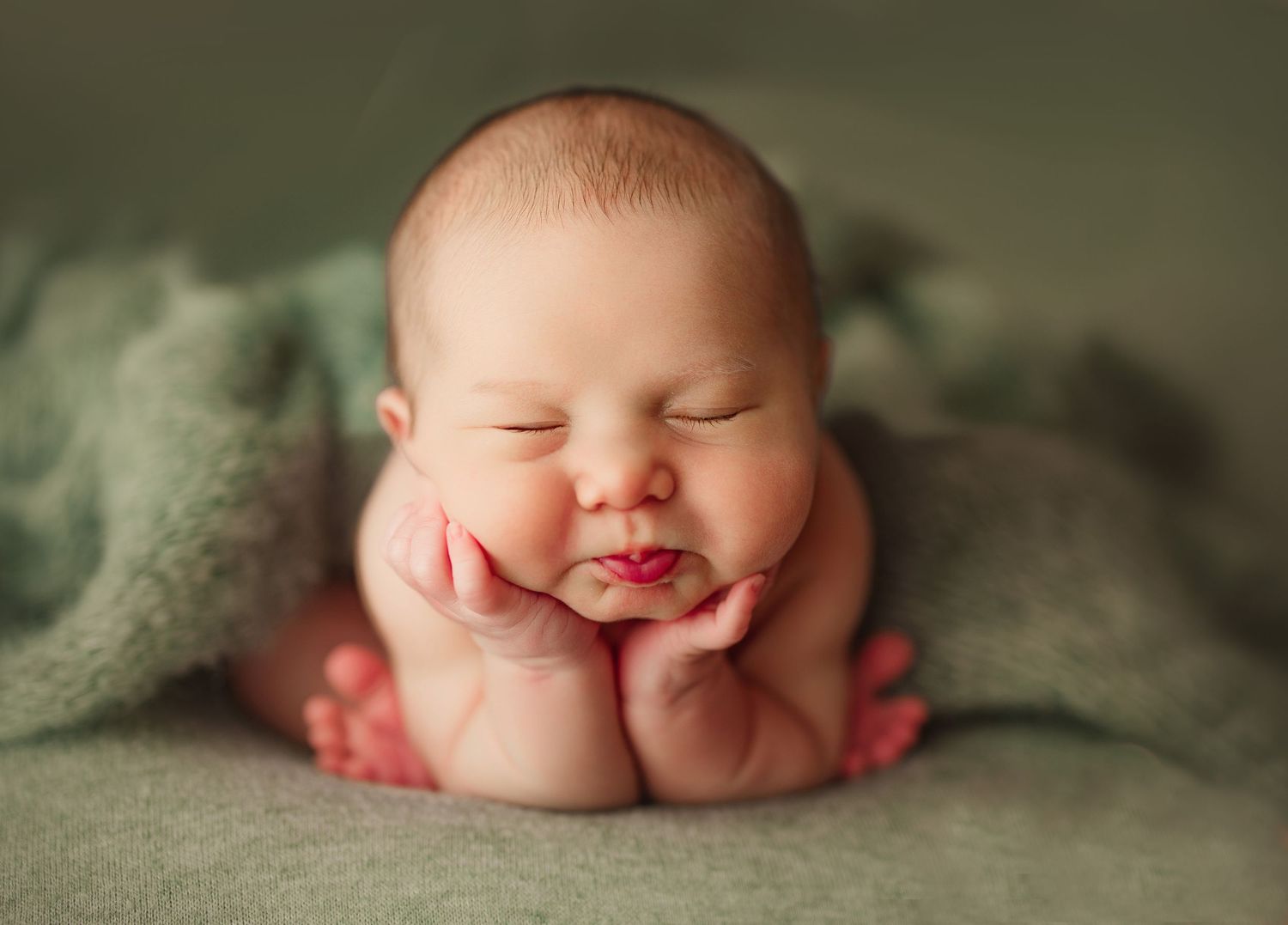 Adorable sleeping newborn baby posed with hands under chin on soft green blanket in professional photography. Richmond VA