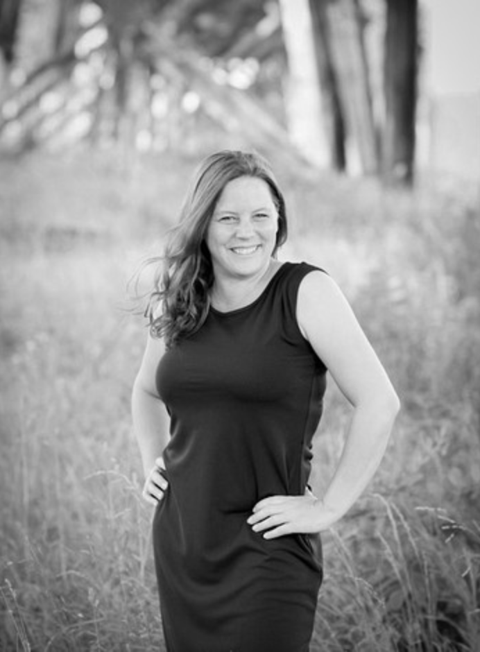 Black and white portrait of a smiling woman in a black dress posing outdoors in a natural field.