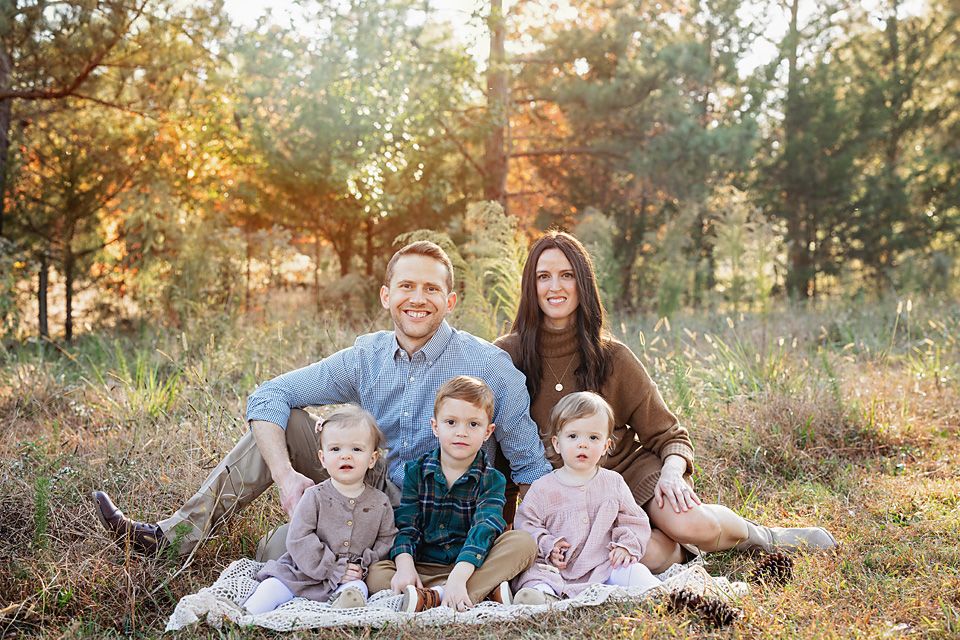 Happy family of five posing together in golden autumn forest setting.