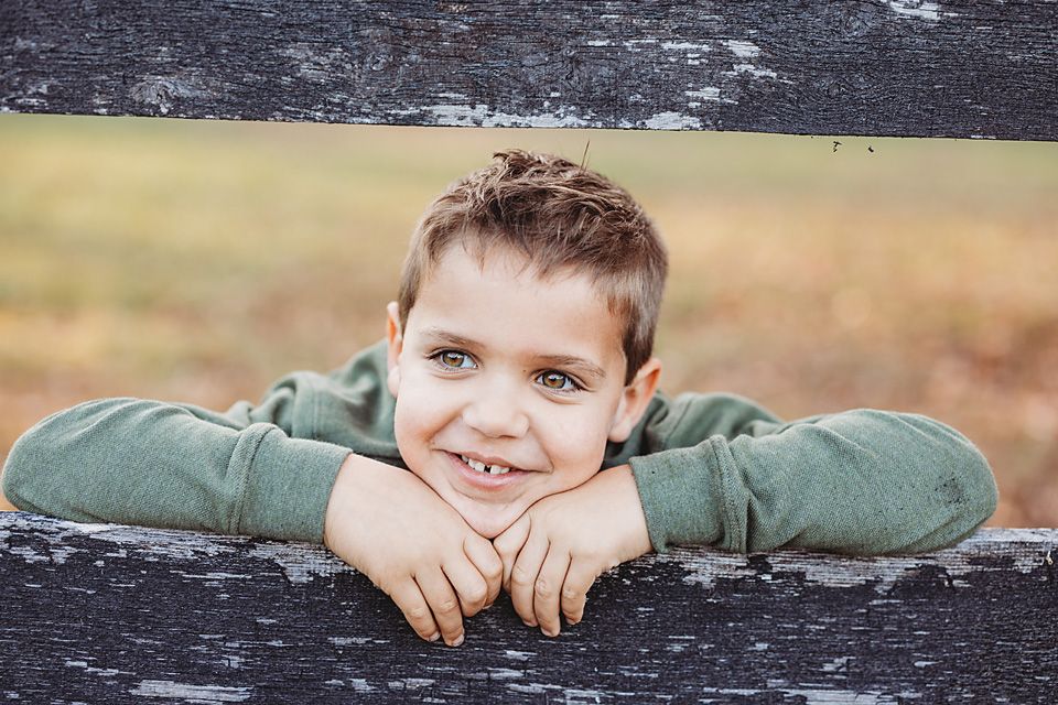 Young boy resting chin on hands on weathered wooden fence. family photography Richmond va