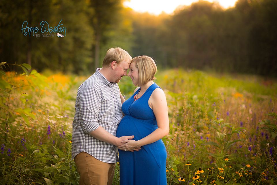 Expectant couple sharing a tender moment in a wildflower field at golden hour, woman in blue dress.