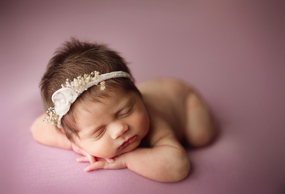 Sleeping newborn baby girl wearing a delicate floral headband, resting peacefully on a soft pink backdrop Richmond newborn photographer