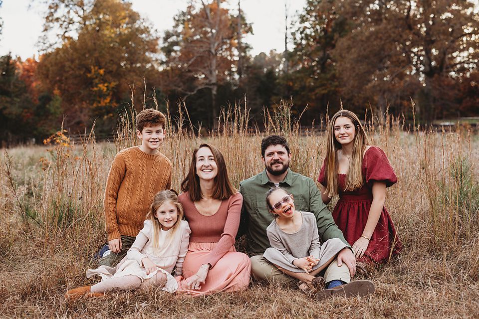 Family of six sitting together in tall golden grass during fall season. photographer