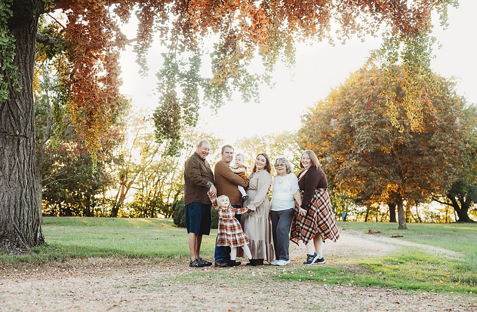 Extended family group posing under colorful autumn tree in park setting.