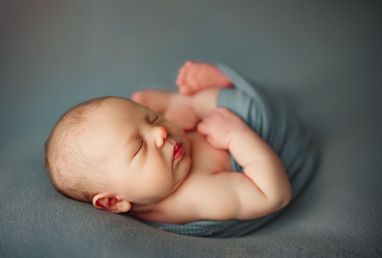 Peaceful newborn baby sleeping curled up on a soft gray blanket in a classic posed newborn photography style. Petersburg newborn photo