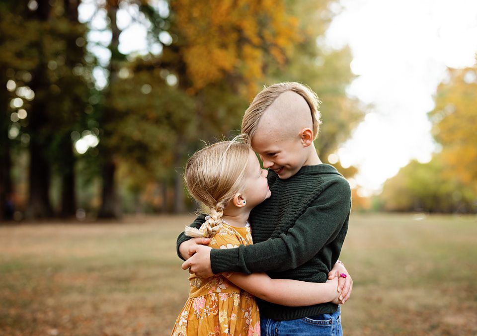 Two young children hugging each other in a colorful autumn park setting.