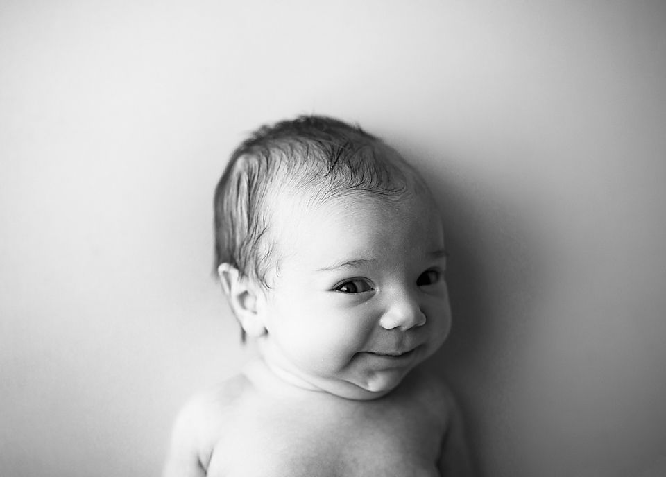 Black and white portrait of smiling baby looking sideways against light background.