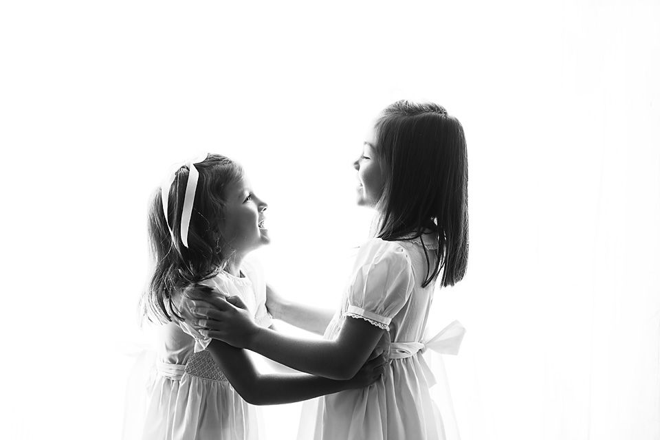 Two young girls in white dresses facing each other in a black and white portrait. children studio photography Chesterfield, midlothian.