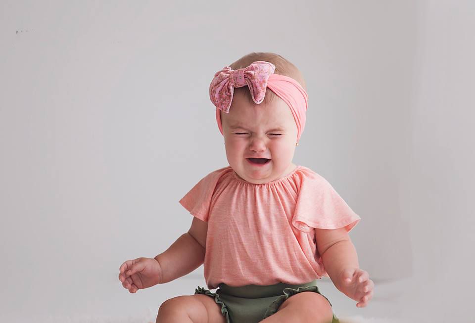 Baby girl in pink flutter sleeve top and bow headband crying during photo session on white backdropRichmond family photographer, midlothian,