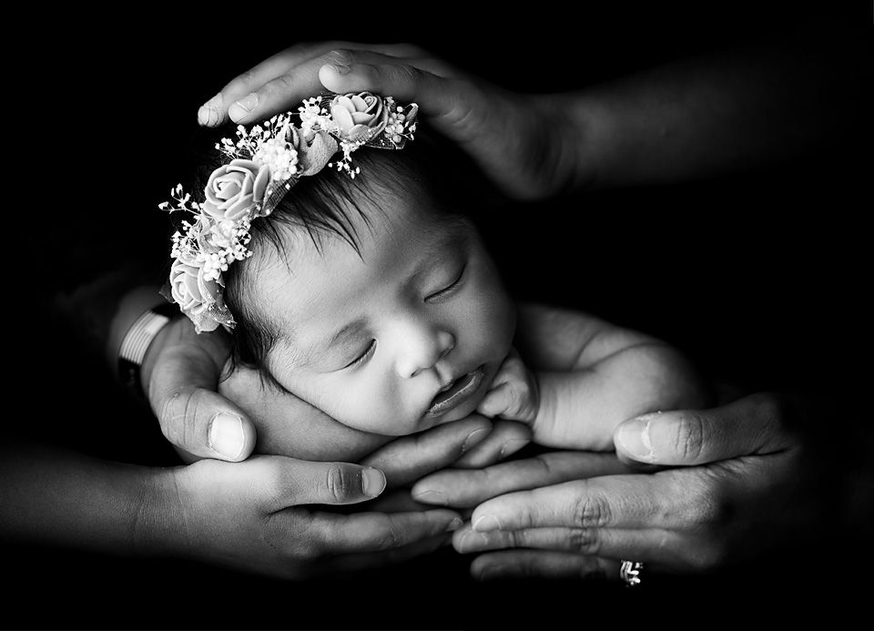 Black and white newborn baby sleeping peacefully in parents hands wearing a delicate floral crown. Newborn photography Petersburg