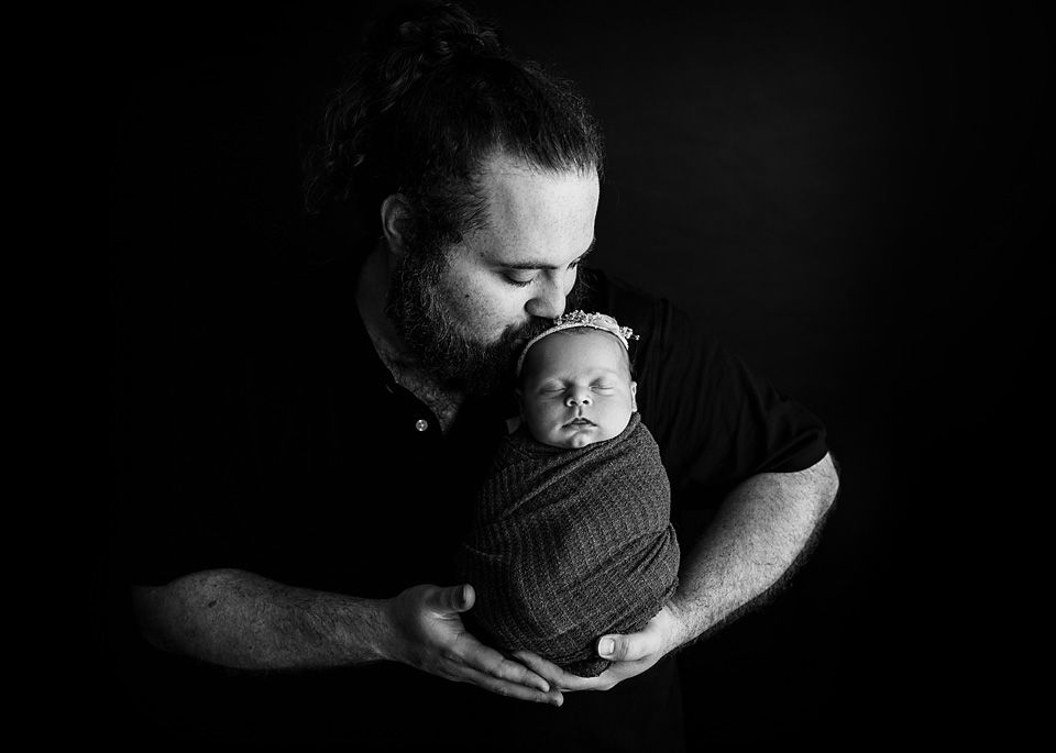 Father kissing swaddled newborn baby in black and newborn photographer Richmond Chesterfield midlothian Petersburg glen Allen short pump