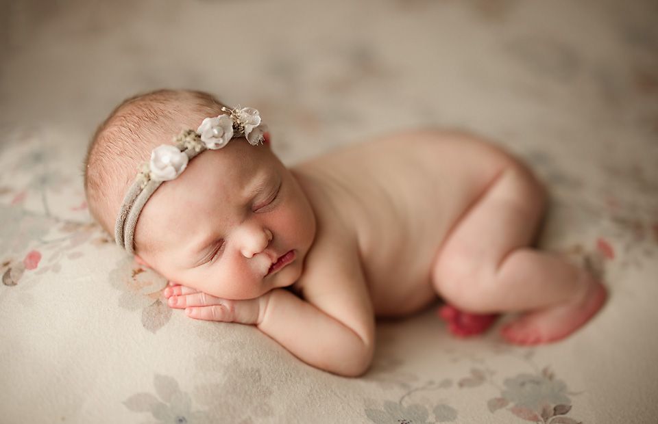 Peaceful sleeping newborn baby with white floral headband lying on soft floral textured blanket.