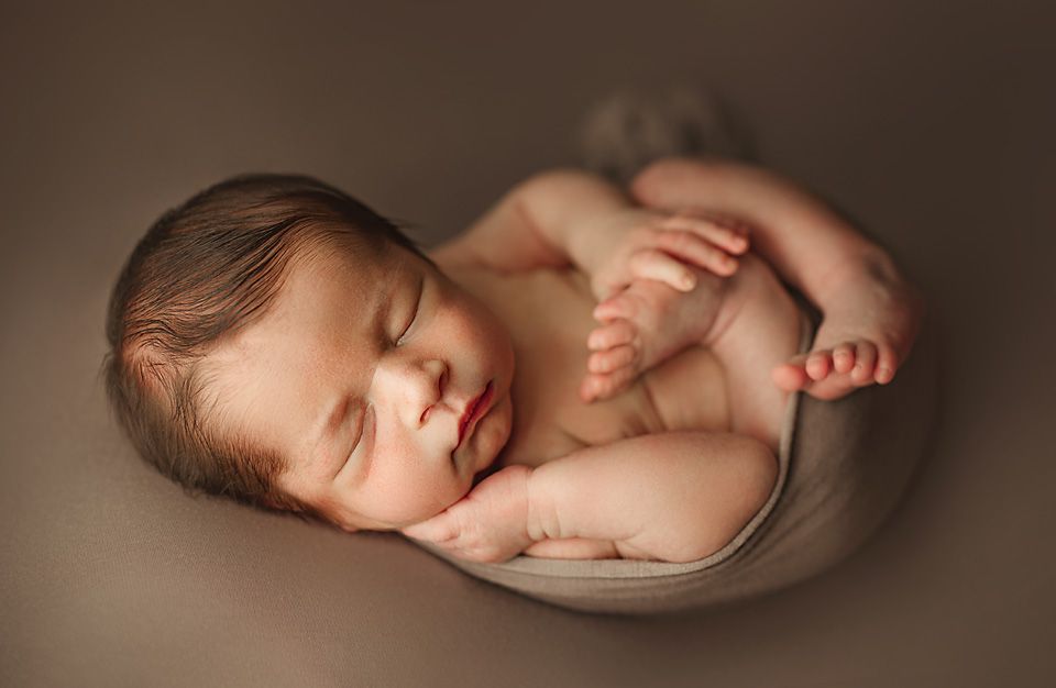 Peaceful sleeping newborn baby curled up on a soft brown textured backdrop.
