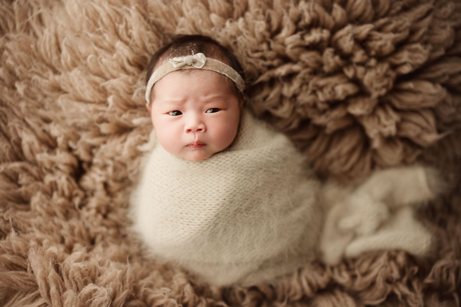Newborn baby wrapped in cream knit swaddle with floral headband, nestled in fluffy brown fur blanketRichmond newborn photographer