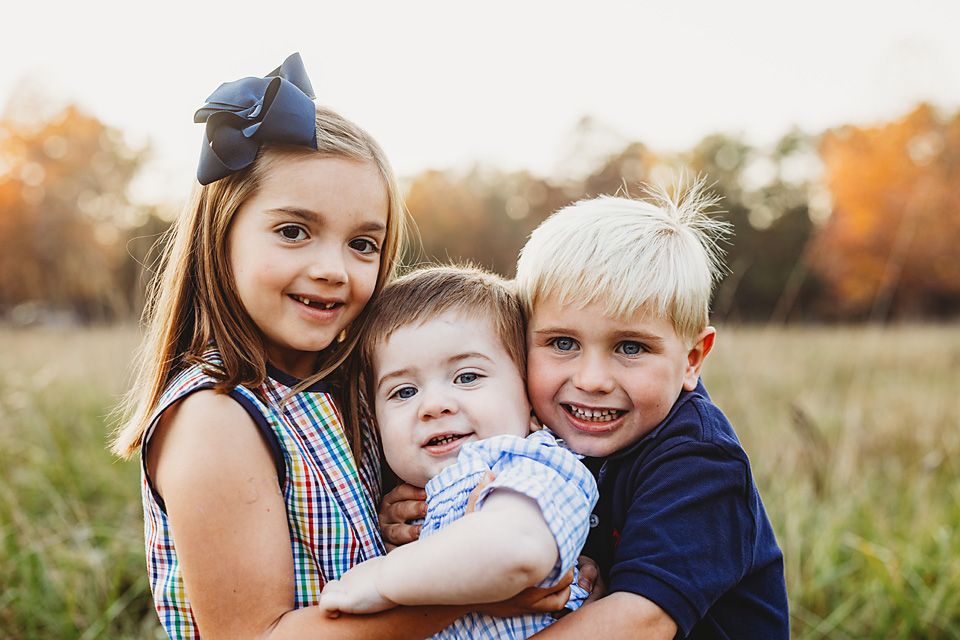 Three young siblings hugging and smiling together in a golden autumn field Richmond VA family photography. Midlothian, Petersburg, Glen Alle