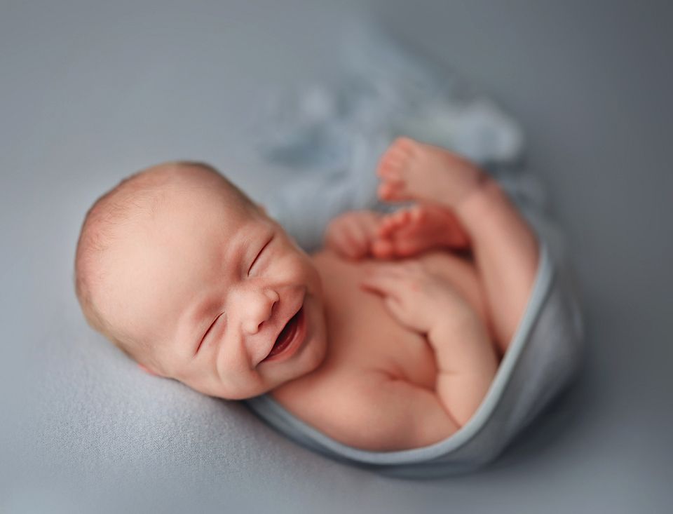Smiling newborn baby wrapped in a soft blue blanket during a professional newborn photography session.