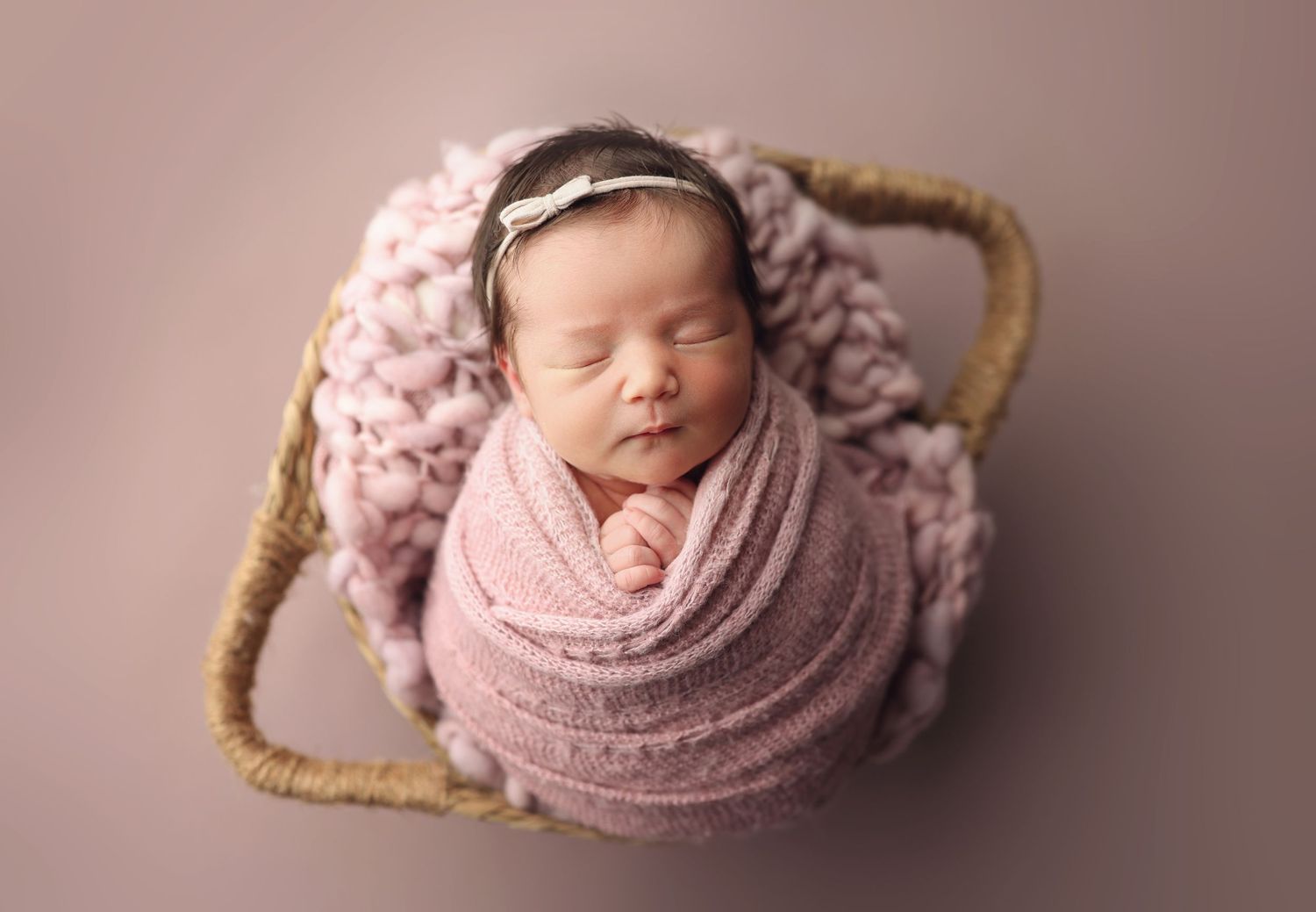 Adorable sleeping newborn baby girl swaddled in pink wrap sitting in a wicker basket.