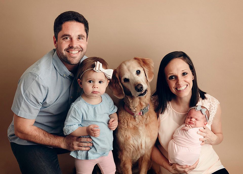 Happy family portrait with dad, toddler girl, golden retriever dog, mom holding newborn baby.