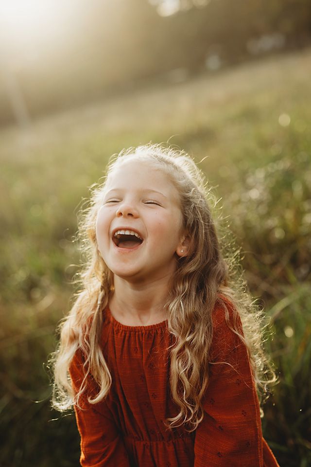 A joyful young girl in a red dress laughs in a sun-drenched autumn meadow.