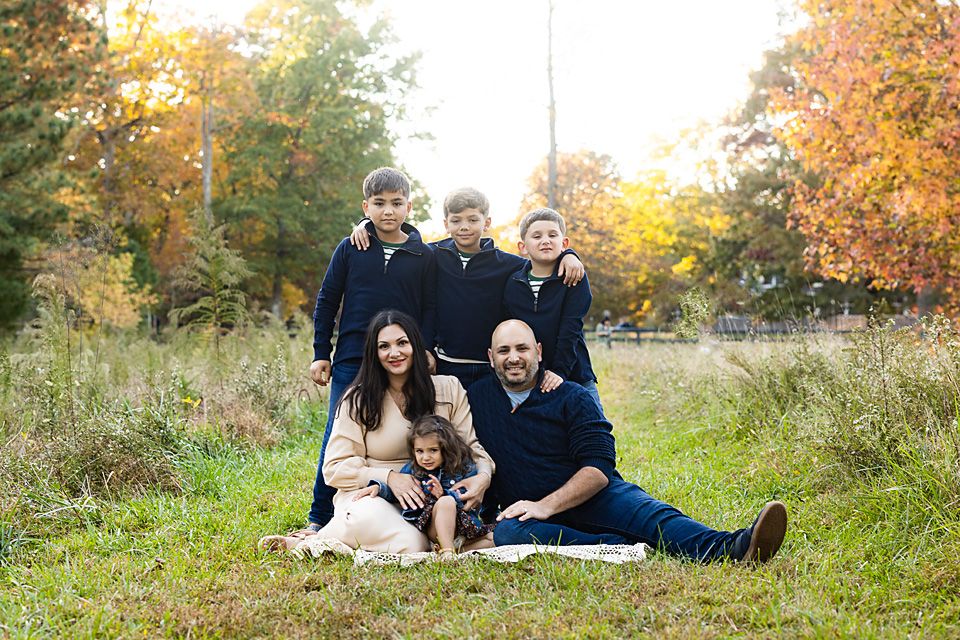 Family of five posing in autumn meadow with colorful fall foliage background. family photographer