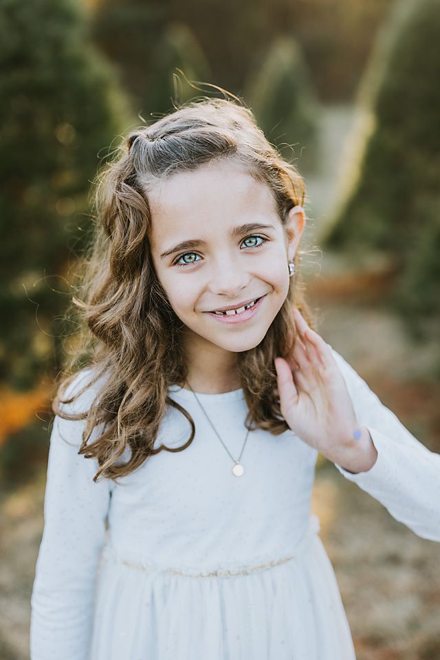 Young girl with curly hair and blue eyes smiling in a white dress outdoors. midlothian children photographer