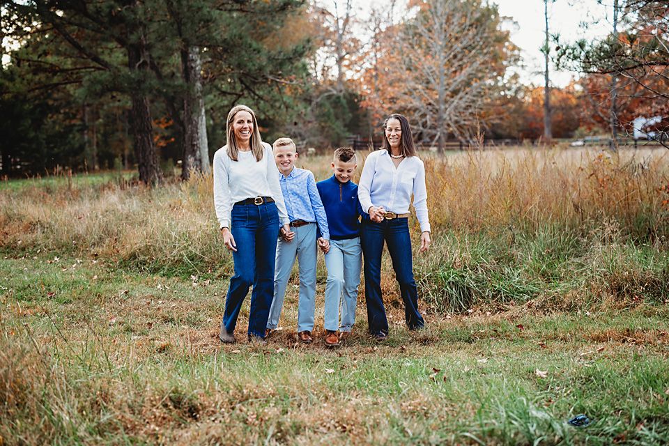 Family of four stands in a golden autumn field, two women flanking two boys in casual coordinated outfits Richmond VA family photography.