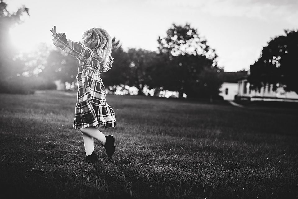 Black and white photo of toddler playing joyfully on green grass in sunlight.
