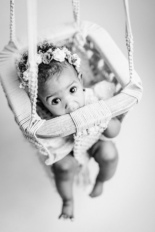 Black and white portrait of a baby girl in a floral crown sitting in a macrame swing.