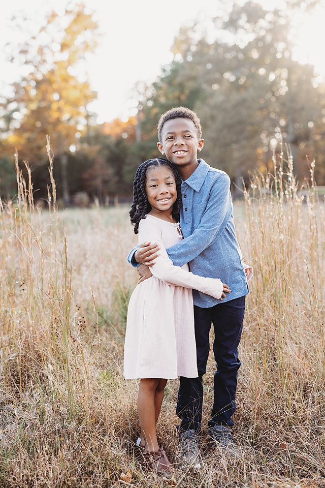 Two children hugging and smiling in a golden field during autumn, boy in blue shirt and girl in pink dress.
Chesterfield family photography