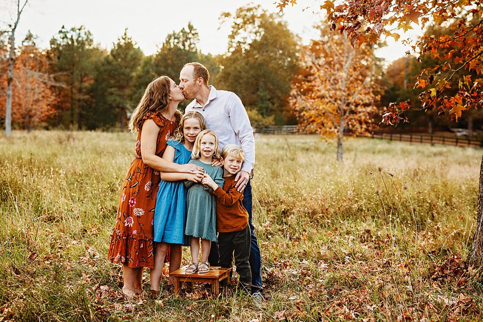 A loving family of five embraces in a colorful autumn field during a fall photo session.