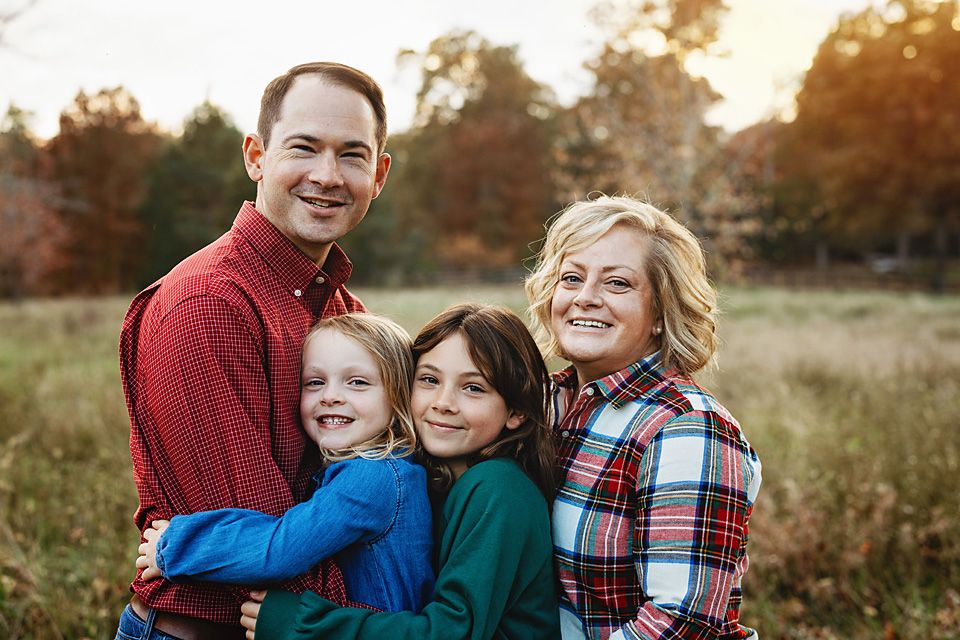 A cheerful family of four hugs together in a fall outdoor portrait session.