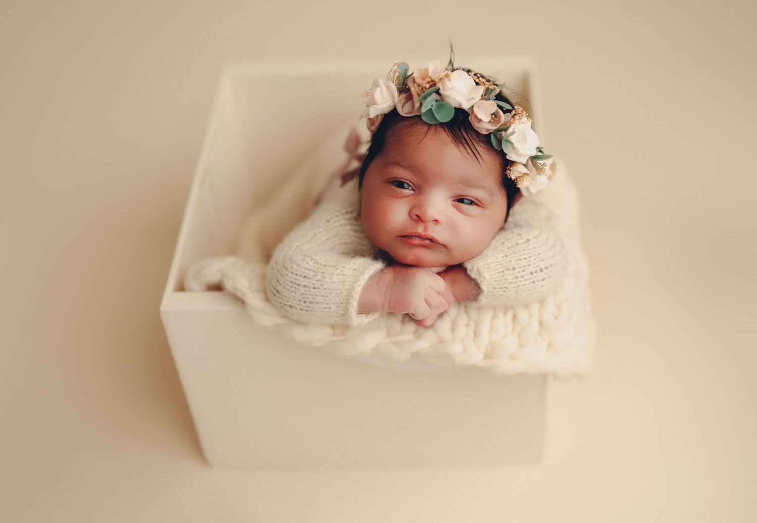 Newborn baby wearing a floral crown nestled in a white box with cream knit wrap, peaceful newborn photography. Richmond newborn photographer