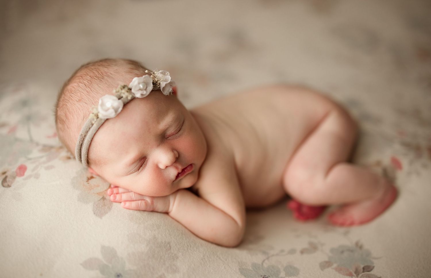 Sleeping newborn baby girl in fetal position wearing floral headband on soft floral blanket Richmond newborn photographer