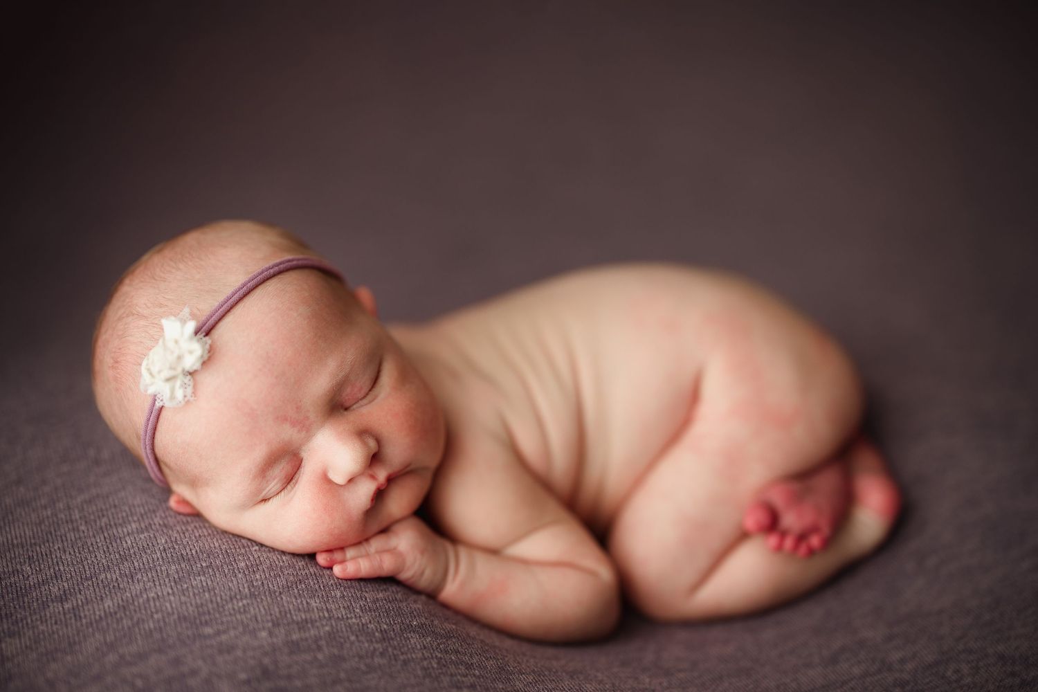 Sleeping newborn baby girl in froggy pose wearing a white flower headband on a gray background. baby photography Richmond