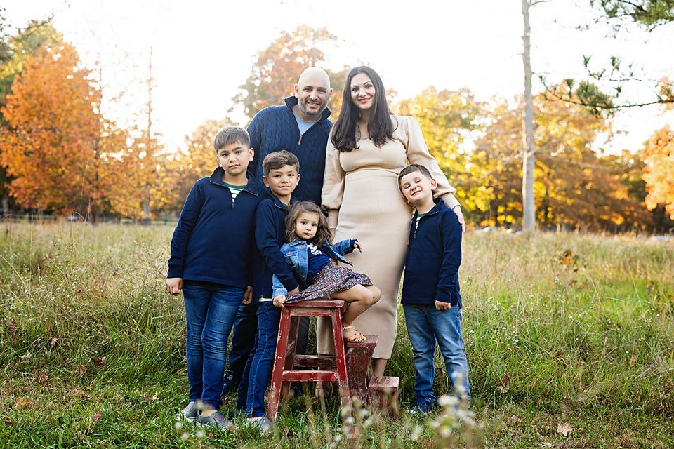 Family of six poses in autumn field, pregnant mother in beige dress with father and three children in navy. Richmond family photographer