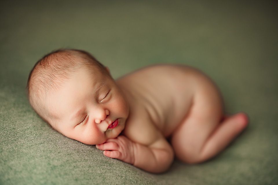 Peaceful newborn baby sleeping curled up on a soft green blanket in a classic froggy pose.Richmond newborn photographer