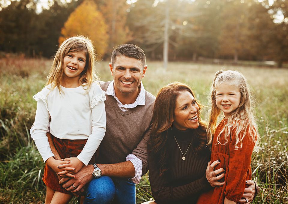 A happy family of four poses together in a sunlit autumn field for a family portrait.