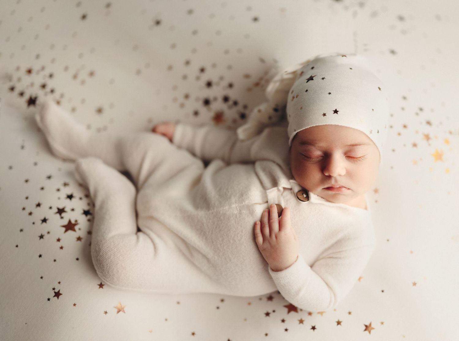 Peaceful newborn baby in a white star-print outfit and hat surrounded by gold star confetti newborn photographer Richmond Chesterfield midlo