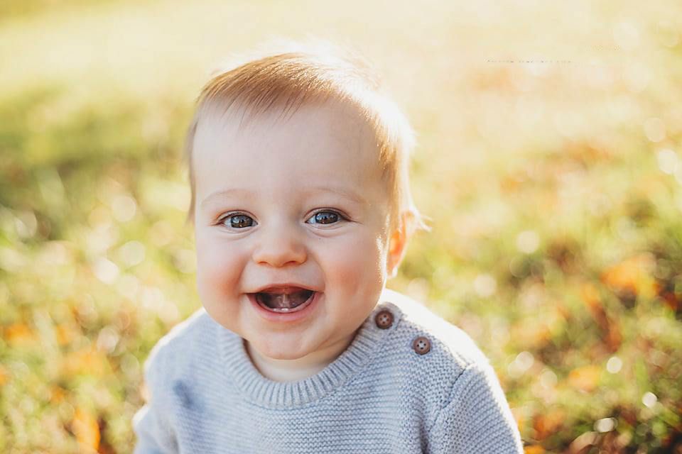 Happy baby boy with two teeth smiling outdoors in a gray sweater in golden sunlight.