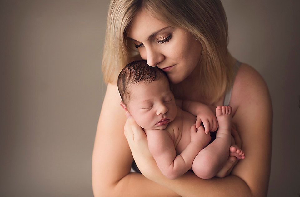 Beautiful young mother gently holding her peaceful sleeping newborn baby close to her chest in a studio portrait.
