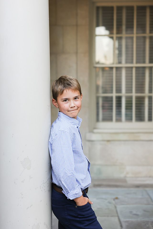 Young boy in a blue checkered shirt leaning against a white column outdoors. Richmond va family photography.